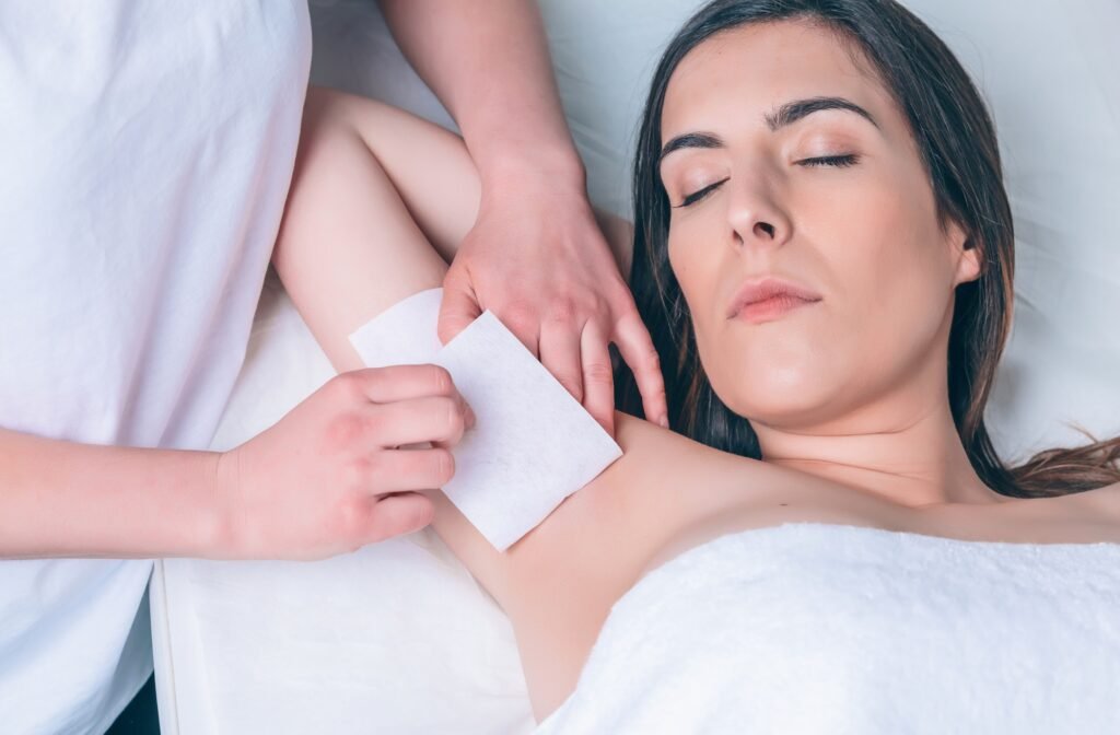 Beautician hands doing depilation in woman armpit with wax strip