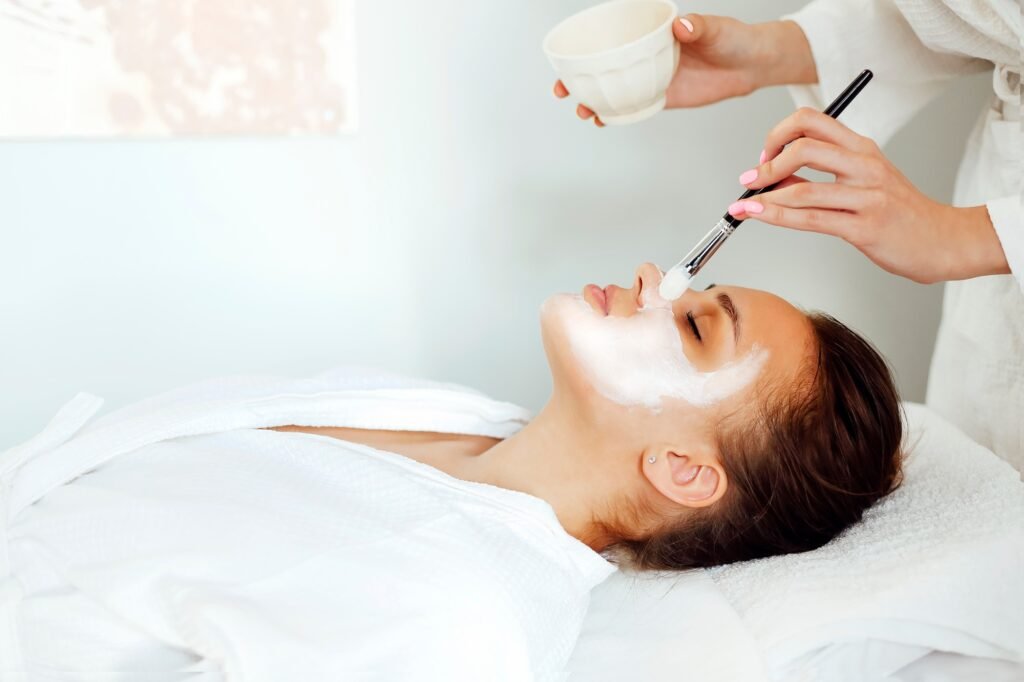 Crop cosmetologist applying facial mask on client